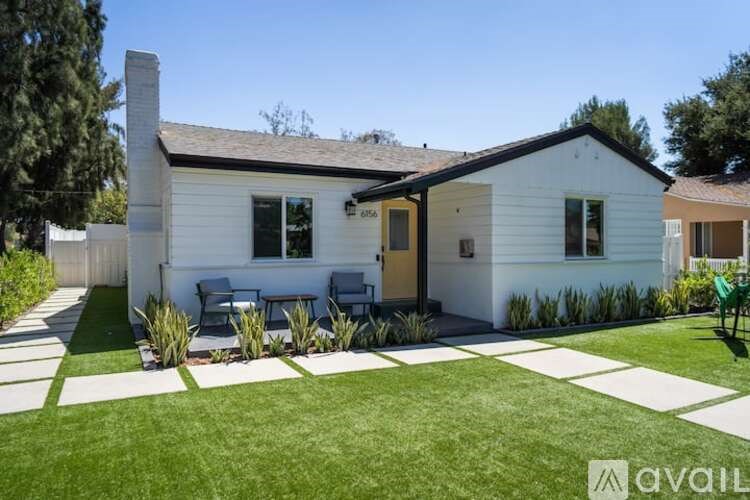 A house with a white exterior and a brown roof has a patio with a table and chairs.