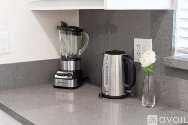 A kitchen counter with a blender, a coffee maker, and a vase with a flower.