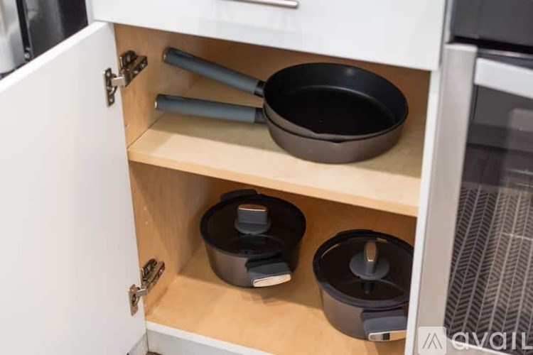 A kitchen cabinet with a black bowl and two black containers on the shelf.