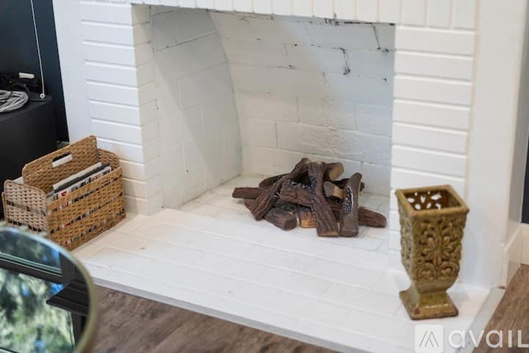 A white fireplace with a basket of logs and a decorative vase on top.