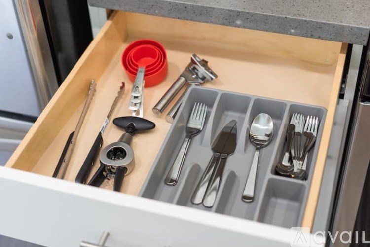 A drawer with utensils and a red object on top.