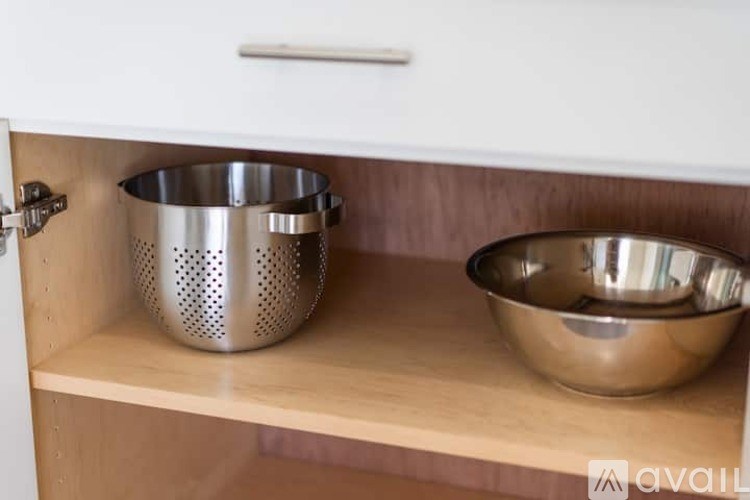 A kitchen cabinet with a silver colander and a bowl on the shelf.