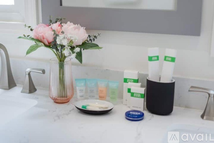 A bathroom sink with a vase of flowers, toiletries, and a mirror.