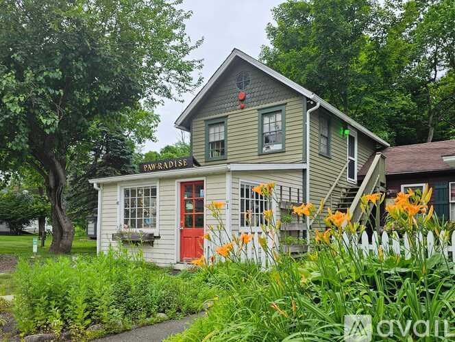 A house with a red door and a sign that says "Paw Paradise" is surrounded by greenery.