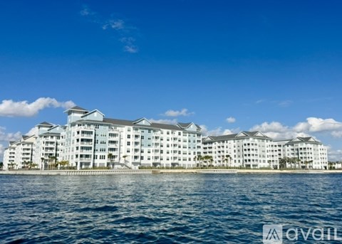 A pool surrounded by lounge chairs and palm trees in front of a white and black apartment building.