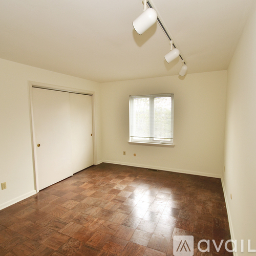 A room with a brown floor and a window with white blinds.