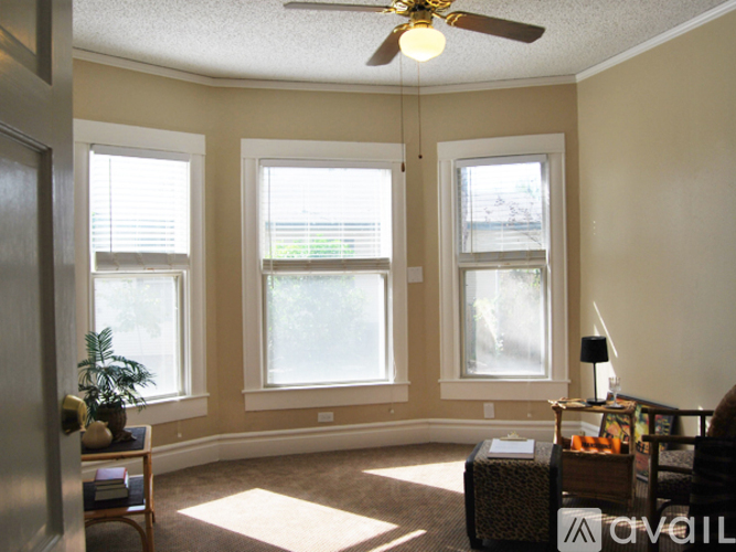 A living room with a ceiling fan and three windows.