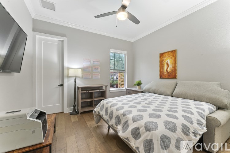 A bedroom with a bed, a desk, a printer, and a ceiling fan.