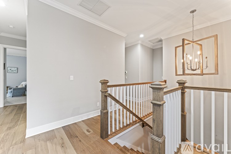 A wooden staircase with a white railing and a chandelier hangs in a room with white walls.