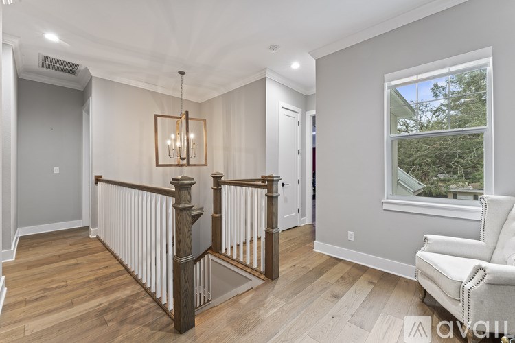 A well-lit room with a wooden floor, a white sofa, and a window showing trees outside.