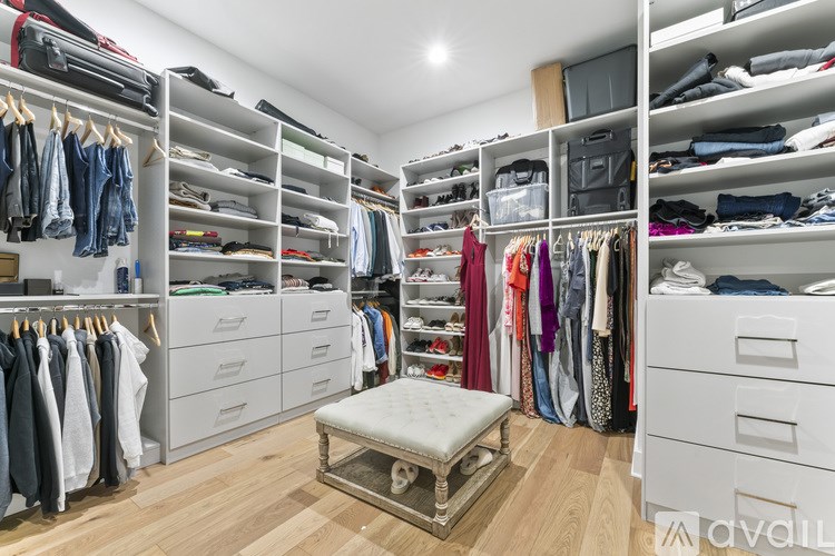 A walk-in closet with white shelving and drawers, filled with clothes and shoes.