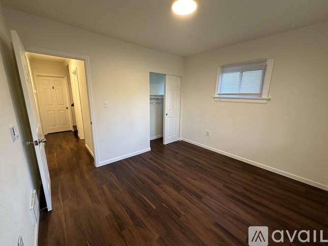 A room with wooden floors and white walls, with a window on the right wall.
