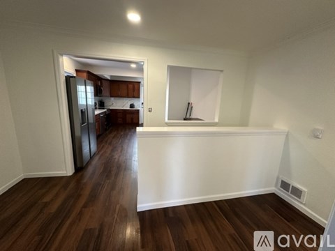 A room with wooden floors and a kitchen area in the background.