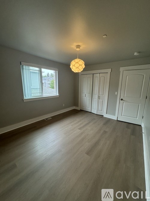 A room with wooden flooring and a window showing a view of a house.