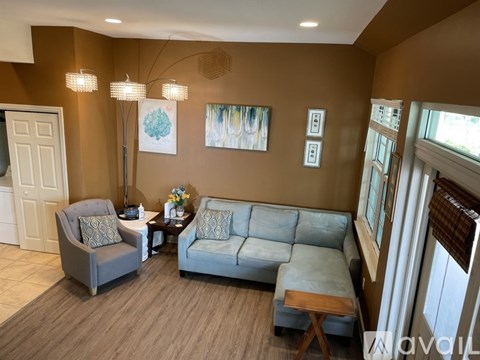 A living room with a grey sofa, a grey armchair, a small table with a vase of flowers, and a painting on the wall.