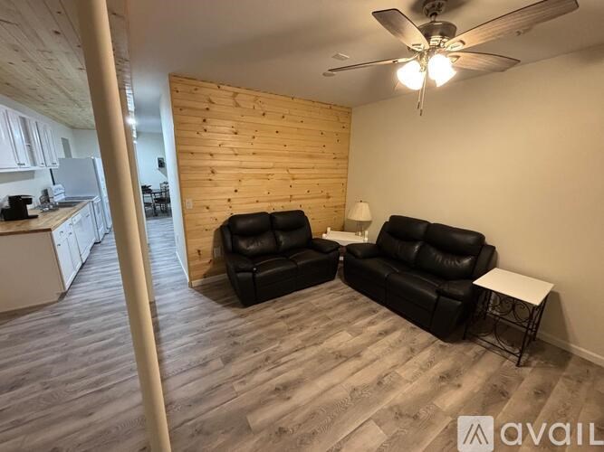 A living room with a black leather couch and a wooden wall.