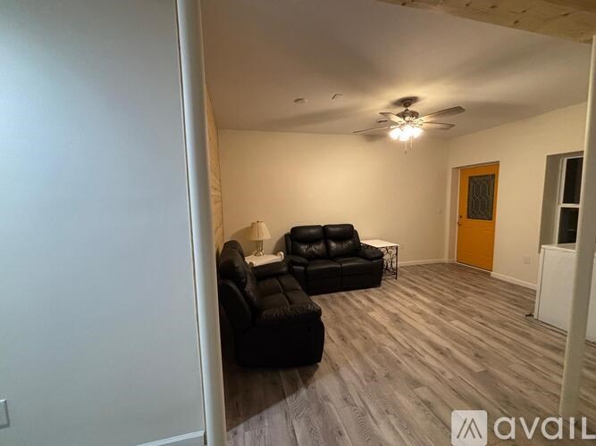 A living room with a black leather couch and a ceiling fan.