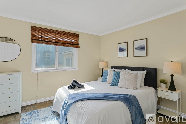 A bedroom with a large bed, a nightstand, and a window with blinds.