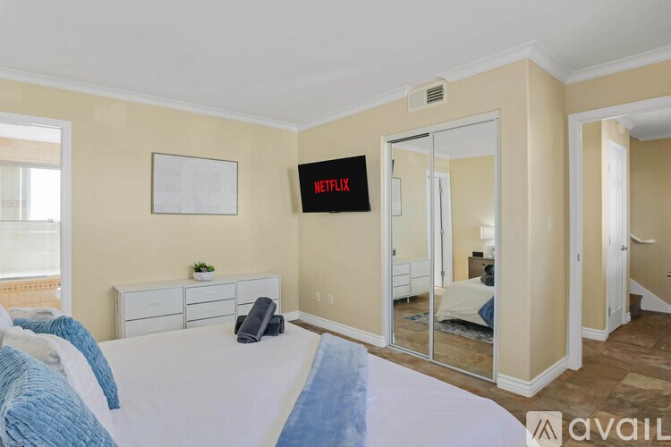 A bedroom with a bed, dresser, and a wall-mounted TV displaying the Netflix logo.