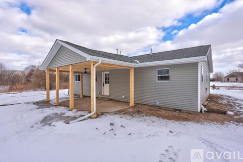 A house with a grey siding and a brown door is surrounded by snow.