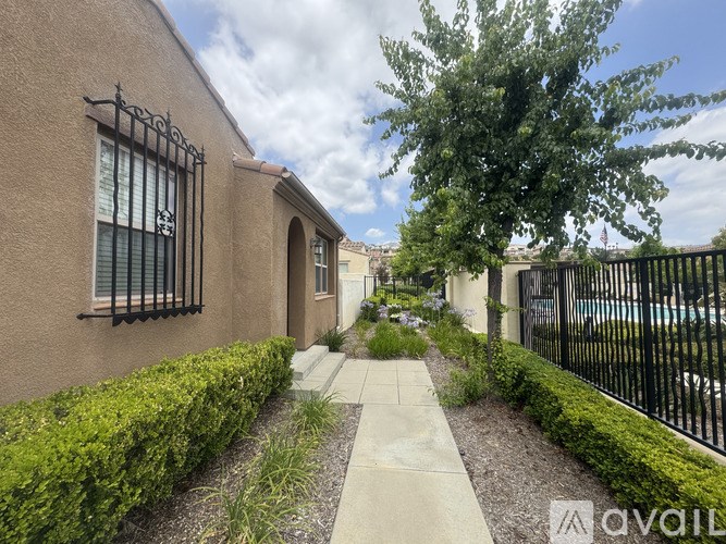 A beige building with a black fence and a tree in front.