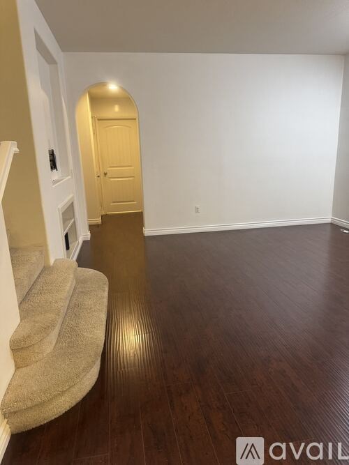 A room with a wooden floor and a staircase with a beige carpet.