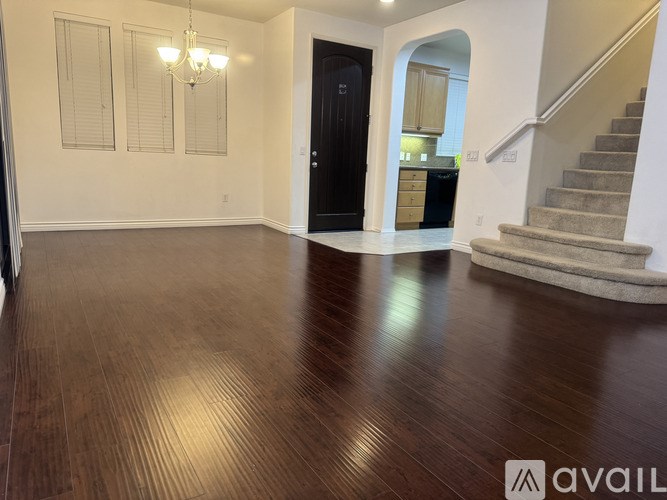 A spacious room with wooden flooring and a staircase leading to another room.