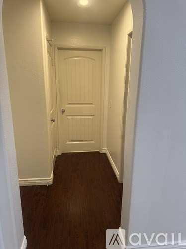 A hallway with a white door and wooden floor.