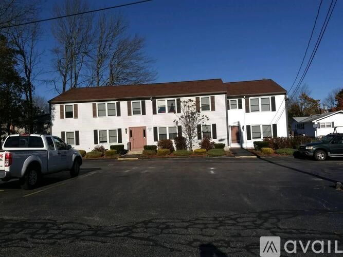 A white building with a brown roof and a parking lot in front.