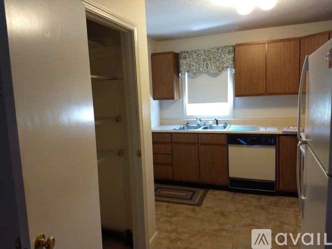 A kitchen with a refrigerator, dishwasher, and a window with a lace curtain.