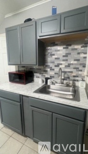 A kitchen with grey cabinets and a marble backsplash.