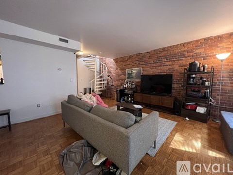 A woman is sitting on a couch in a living room with a brick wall.