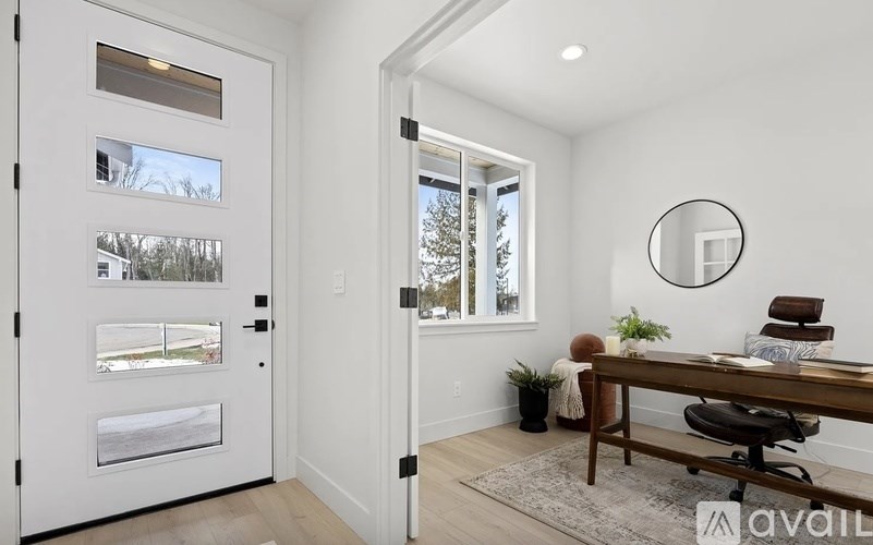 A white door with a glass window is on the left and a wooden desk with a chair is on the right.