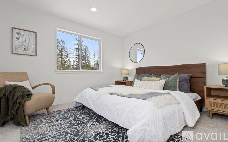 A bedroom with a large bed, a chair, and a window overlooking a forest.