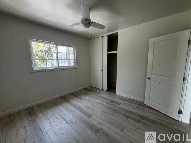 A room with a ceiling fan and a window with a view of trees.