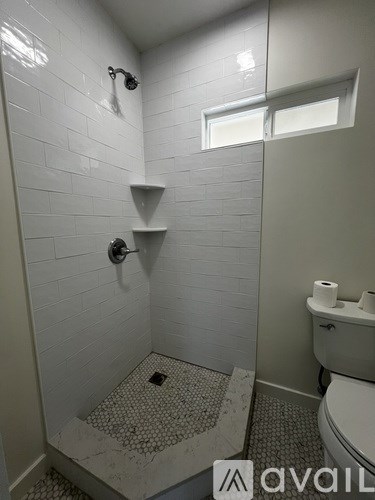 A bathroom with a toilet, a shower with a glass door, and a window.