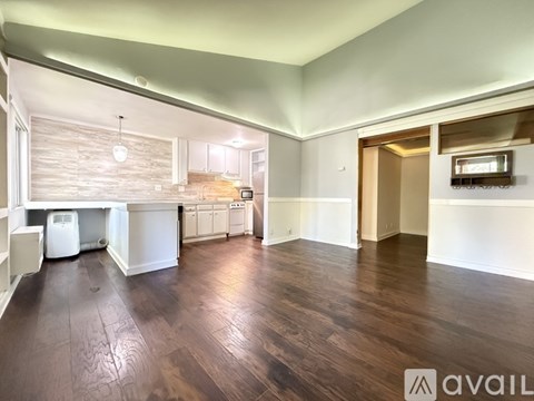 A spacious living room with wooden floors and a kitchen area in the background.