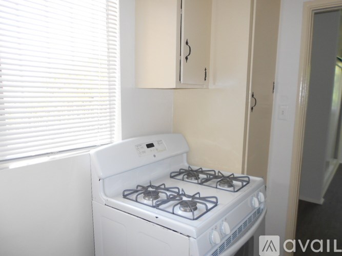 A white gas stove in a kitchen with beige cabinets and a window with blinds.