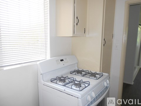 A white gas stove in a kitchen with beige cabinets and a window with blinds.