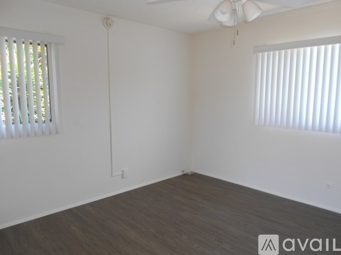 A room with wooden flooring and two windows with blinds.