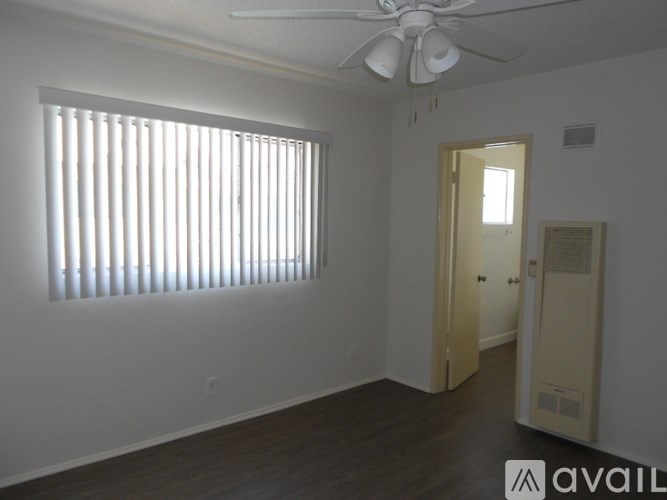 A room with a fan, wooden floor and a door.