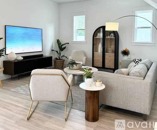 A modern living room with a grey sofa, a white chair, and a TV on a wooden cabinet.
