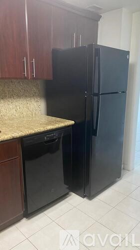 A black refrigerator in a kitchen with brown cabinets.