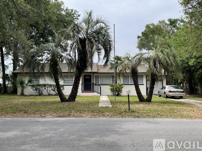A house with a car parked in front and palm trees in front of it.
