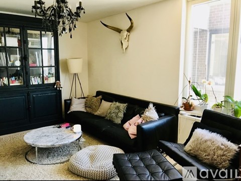 A person is sitting on a black leather couch in a living room with a deer skull on the wall.