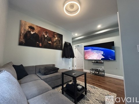 A living room with a grey couch, a black coffee table, and a painting on the wall.