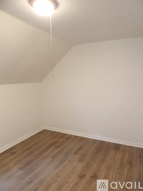 A room with wooden flooring and a single light hanging from the ceiling.