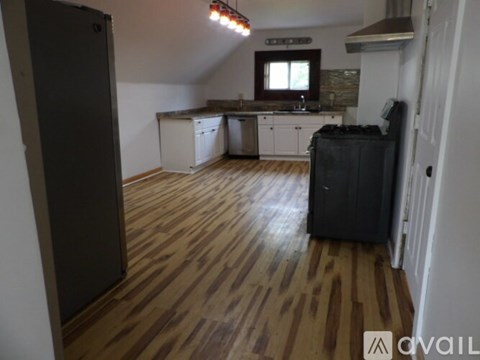 A kitchen area with a black fridge, wooden flooring, and a window.