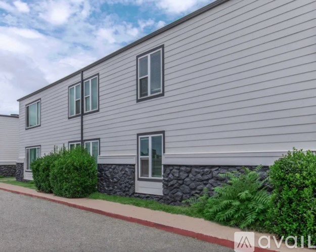 A building with grey siding and a white door is surrounded by greenery.