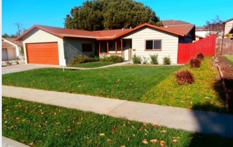A house with a red garage door is surrounded by a green lawn.